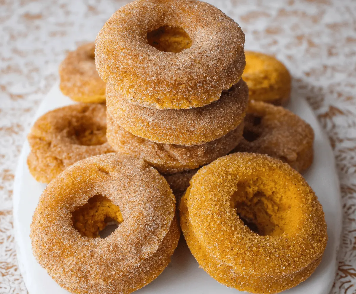 Delicious baked pumpkin spice donuts topped with cinnamon and powdered sugar on a rustic plate, perfect for fall desserts.