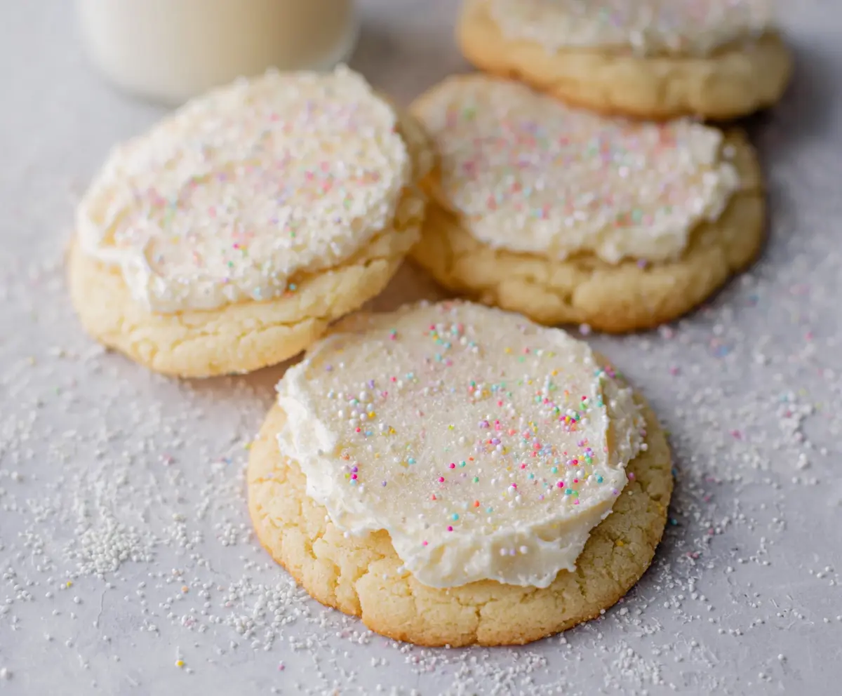 Delicious Crumbl Vanilla Sugar Cookies on a plate with sprinkles and a glass of milk