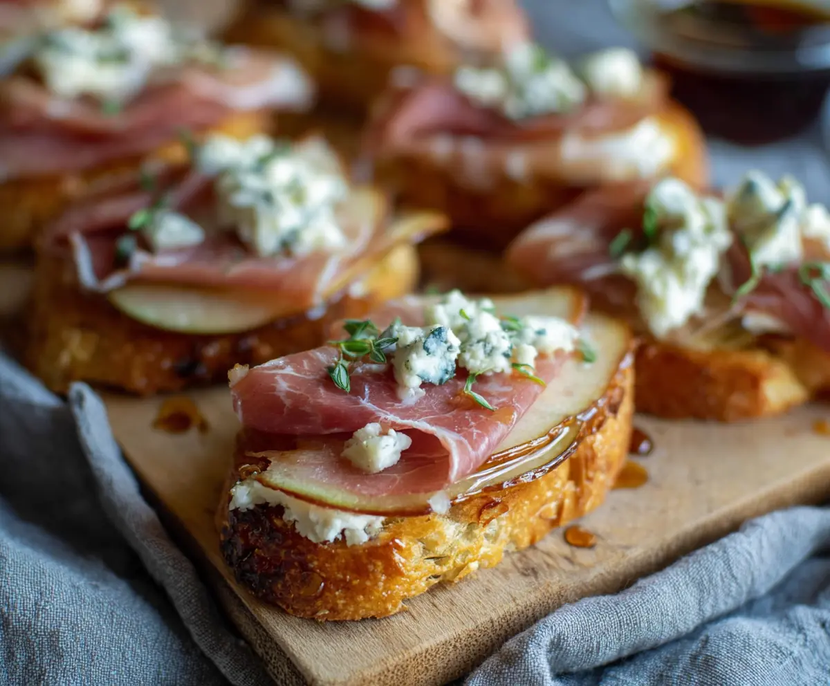 Delicious Prosciutto Pear Gorgonzola Crostini served on a platter with fresh herbs.