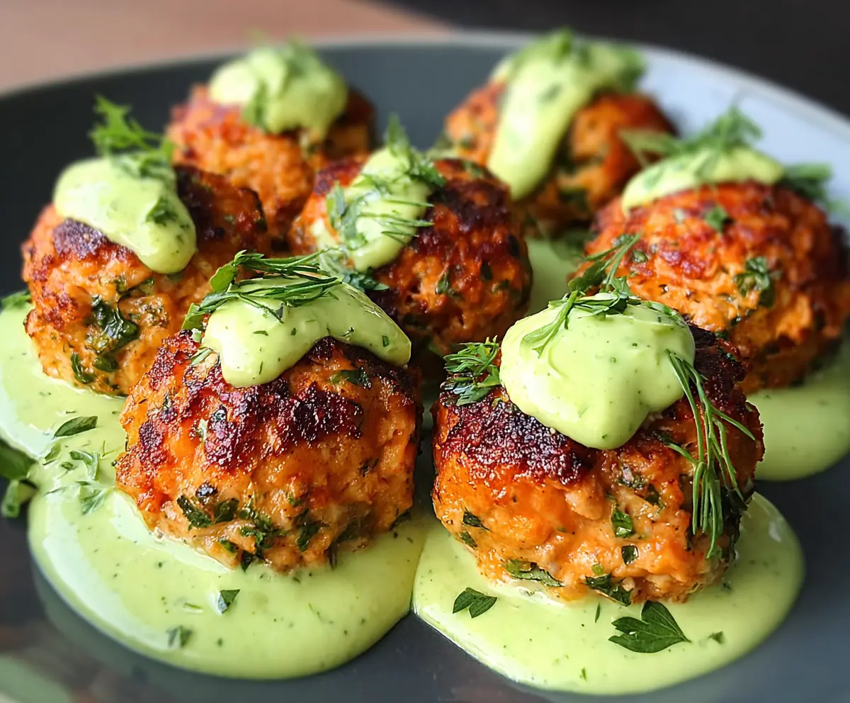 Delicious baked salmon meatballs served with a tangy avocado sauce on a white plate.