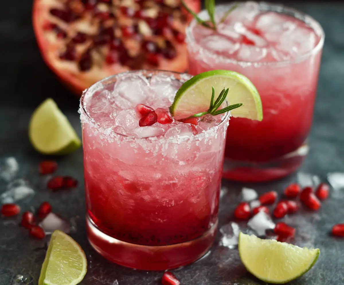 A refreshing Pomegranate Paloma cocktail in a glass garnished with pomegranate seeds and a lime wedge.