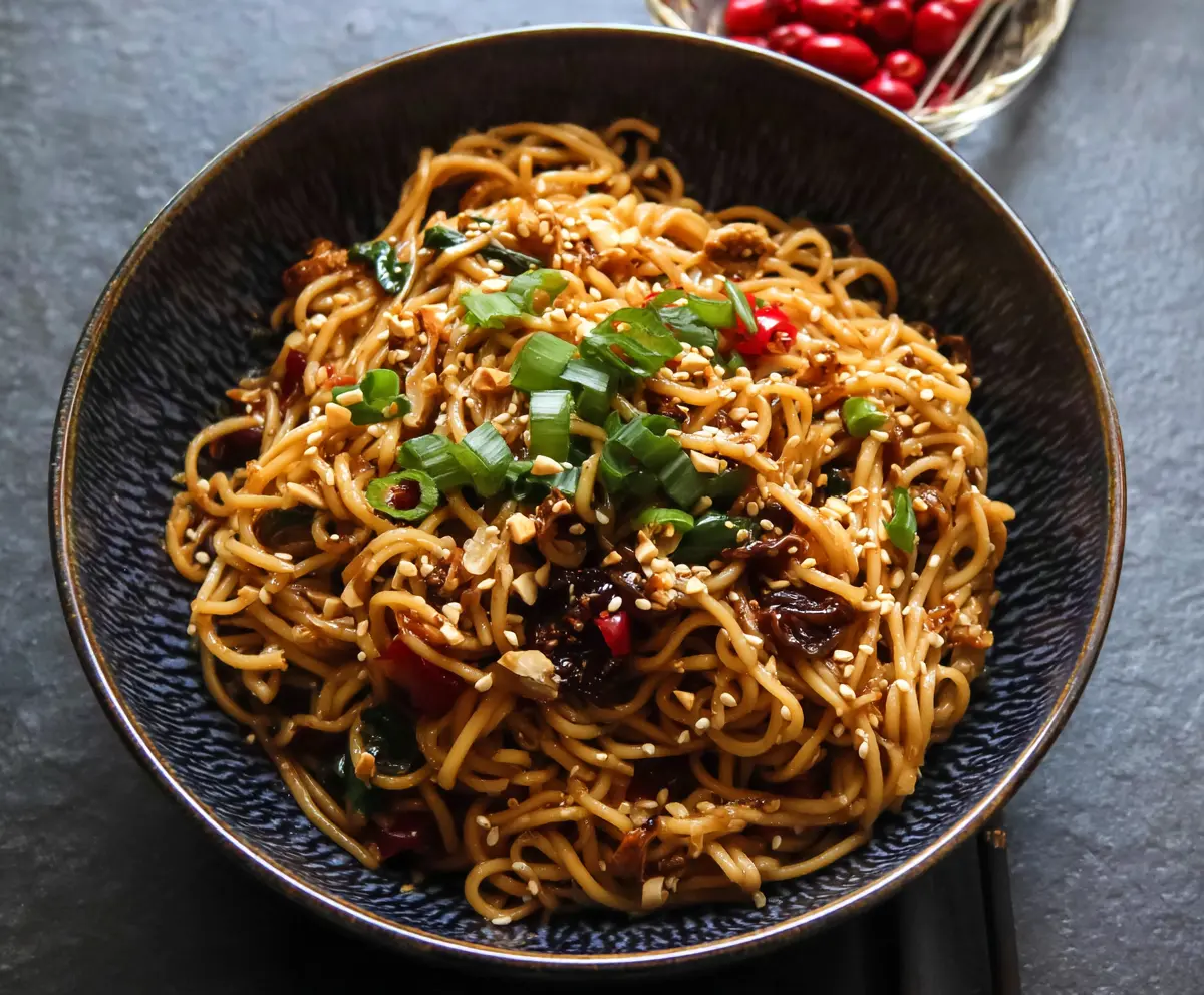 Delicious spicy sesame noodles garnished with sesame seeds and green onions.