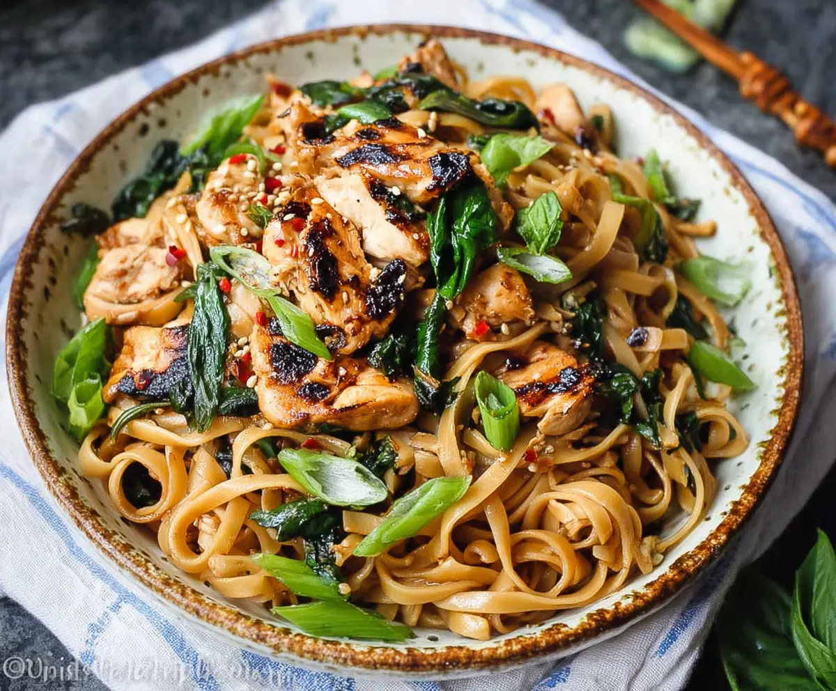 Delicious Thai Basil Chicken Noodles in a bowl garnished with fresh herbs and peppers.