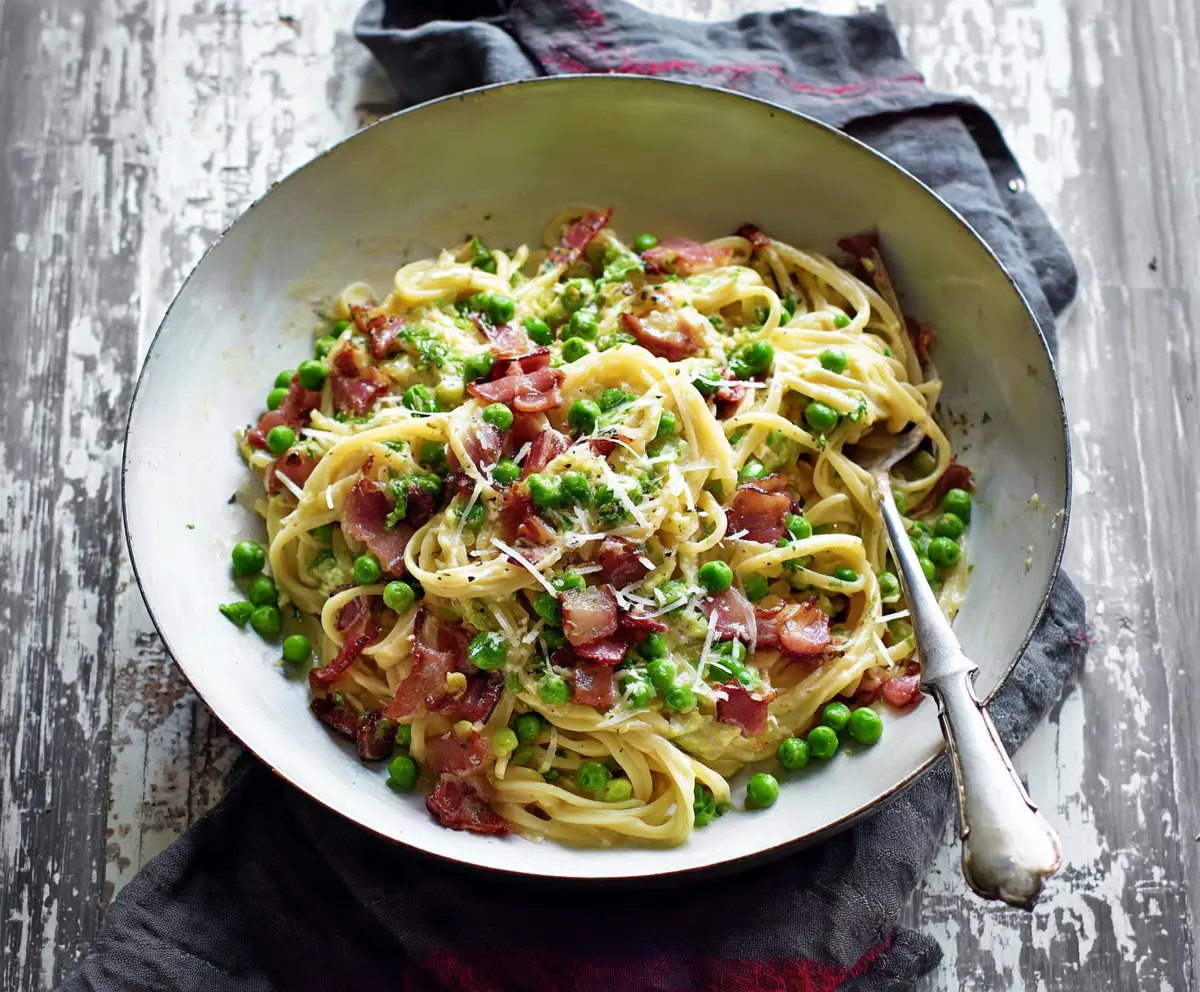 Delicious bacon and pea pasta dish garnished with fresh herbs, served on a white plate.