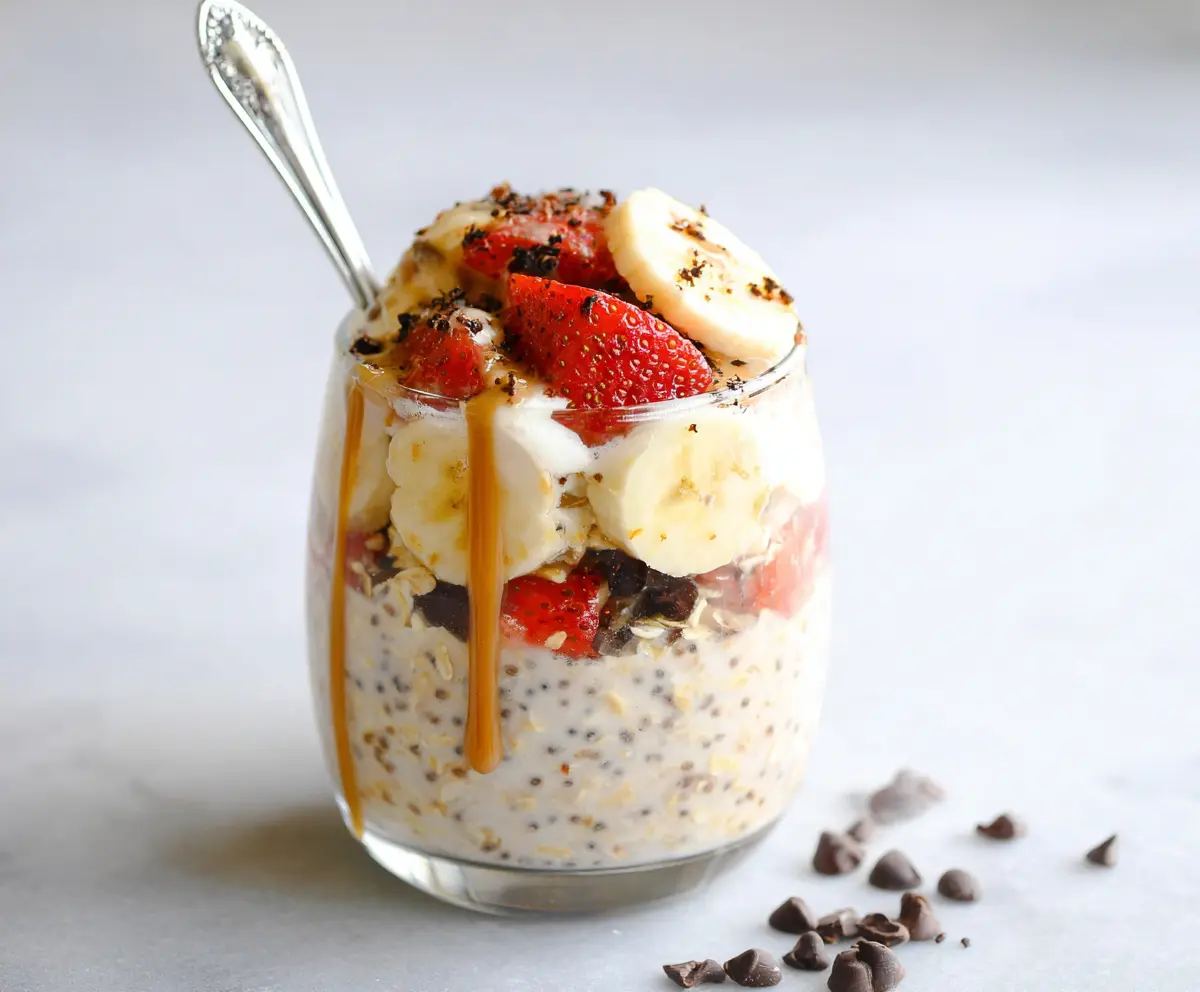 Delicious banana split overnight oats topped with fresh bananas and chocolate syrup in a glass jar.