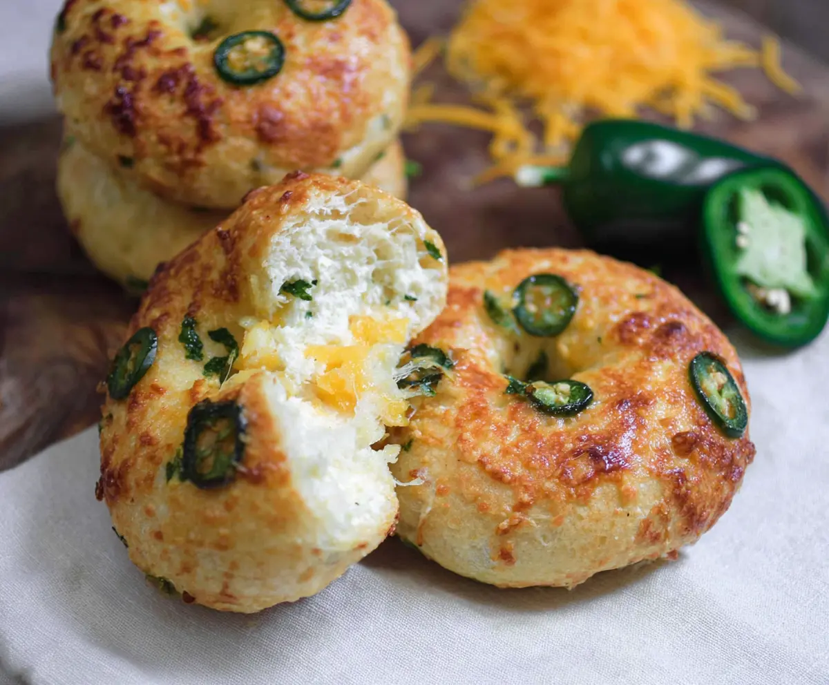 Delicious Cottage Cheese Jalapeño Cheddar Bagels on a wooden board with fresh herbs.