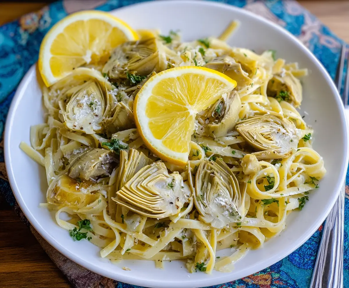 Delicious lemon artichoke pasta garnished with fresh herbs on a white plate.