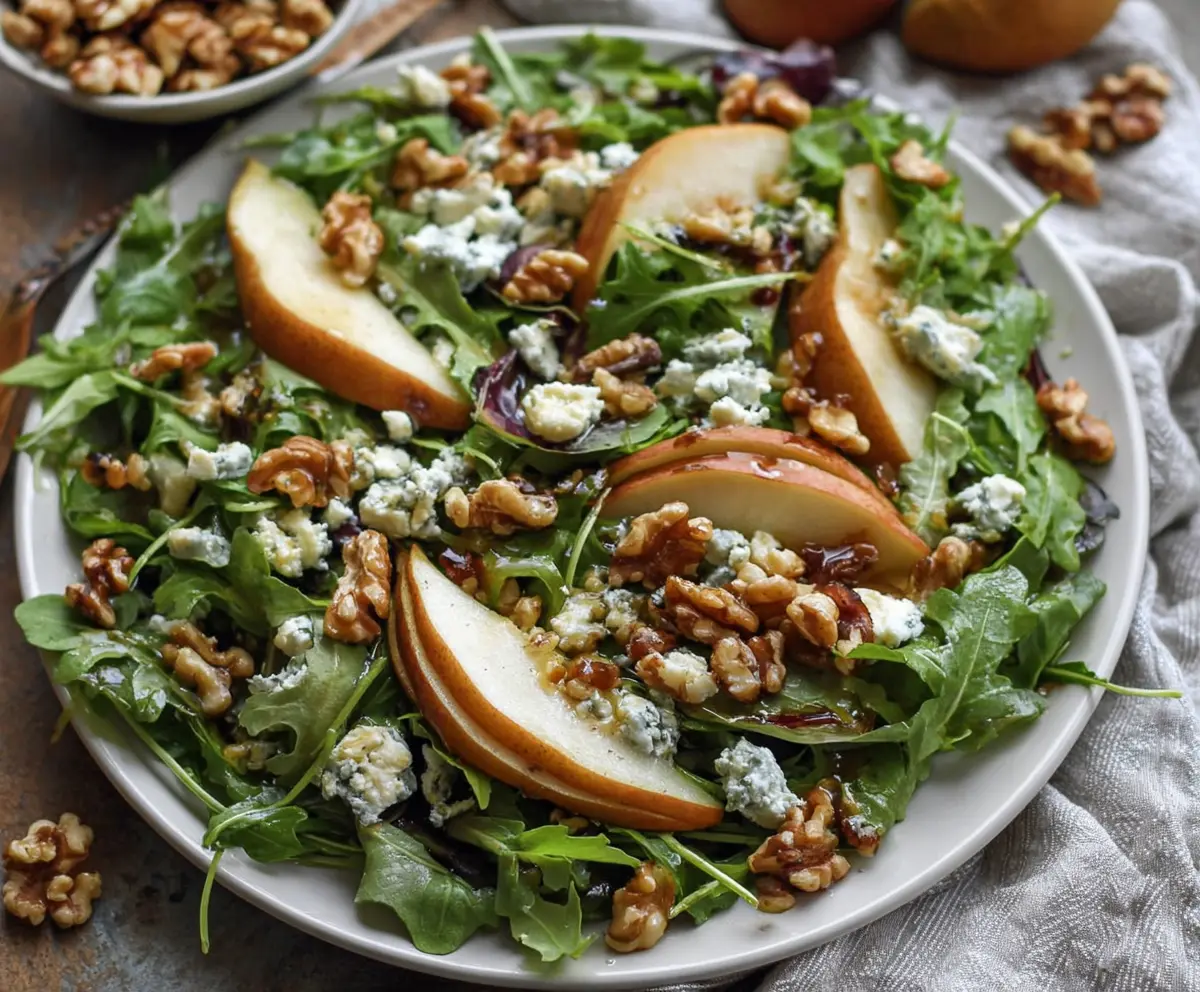 Fresh arugula and ripe pears salad with crumbled blue cheese and walnuts on a white plate.