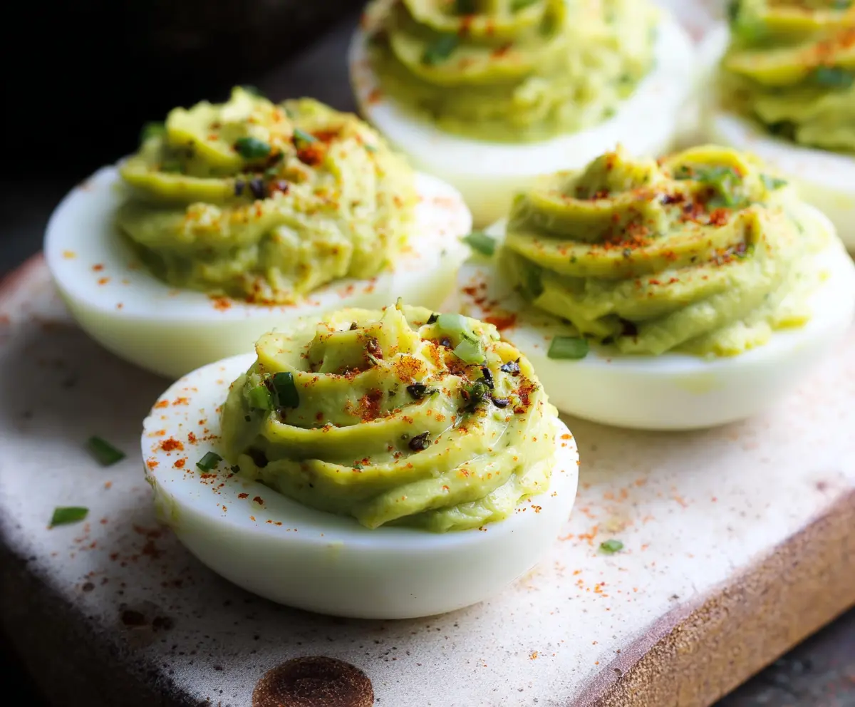 Creamy avocado-filled deviled eggs topped with herbs on a white plate, perfect for healthy appetizer recipes